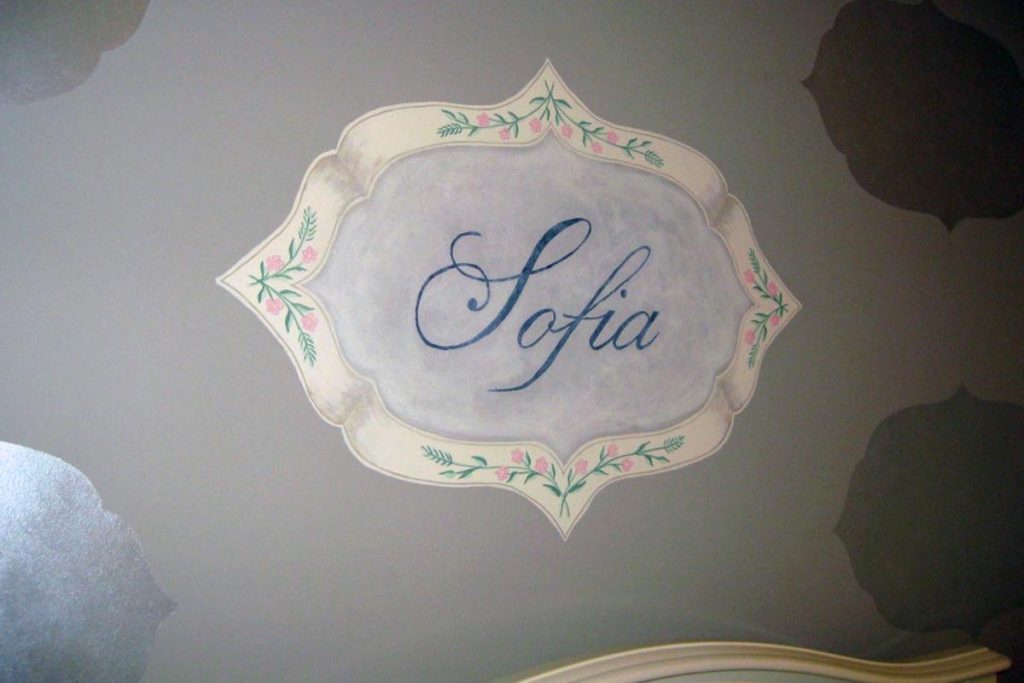Hand-painted decorative frame with baby’s name painted over the crib, and iridescent silhouettes of frame shape painted throughout room.