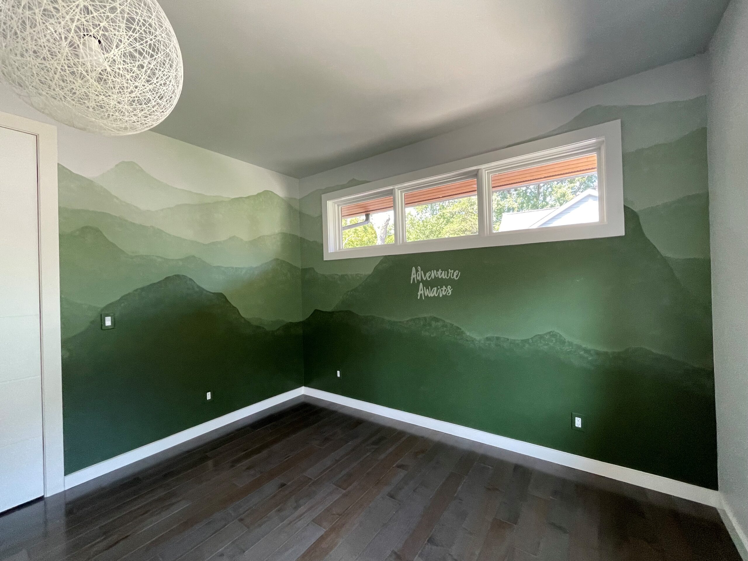 "Adventure Awaits" nursery mural with soft graphic mountain range in shades of green.