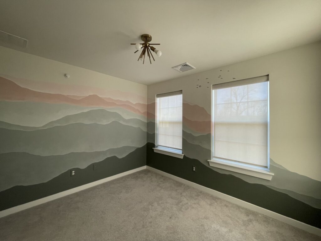 Nursery mural painted with gradient mountain range in greens and coral with a flock of birds.