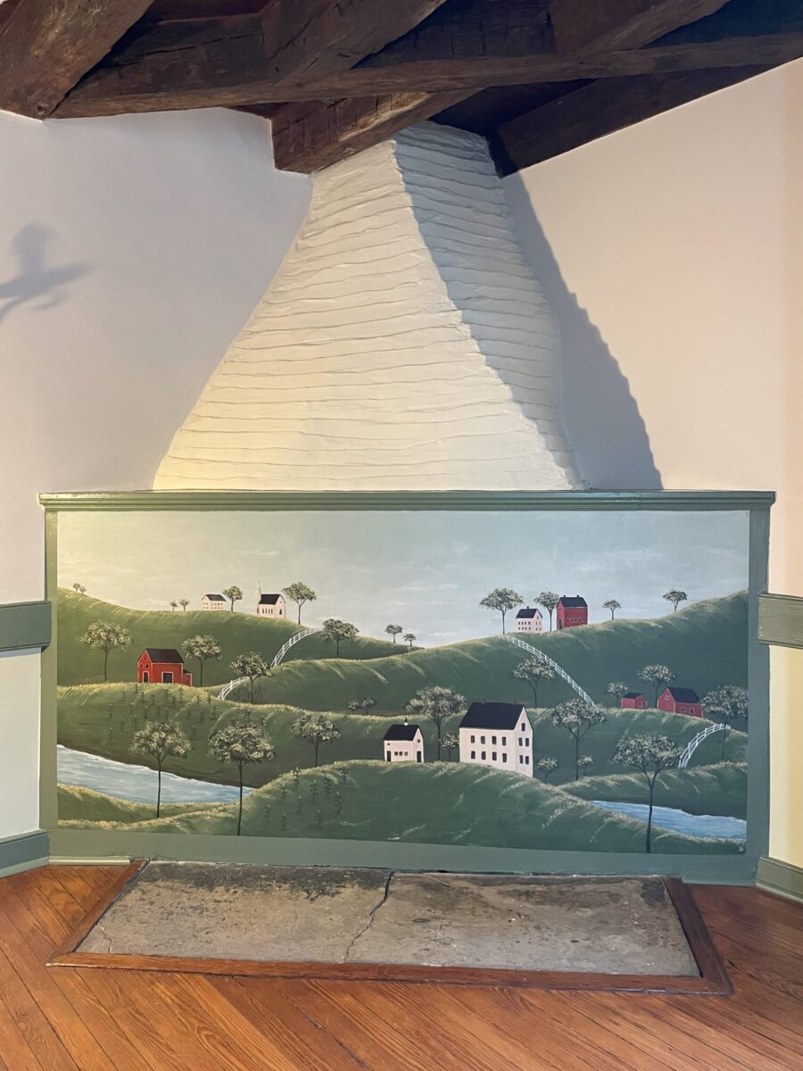 Folk Art style landscape mural painted on blocked fireplace in historic home.