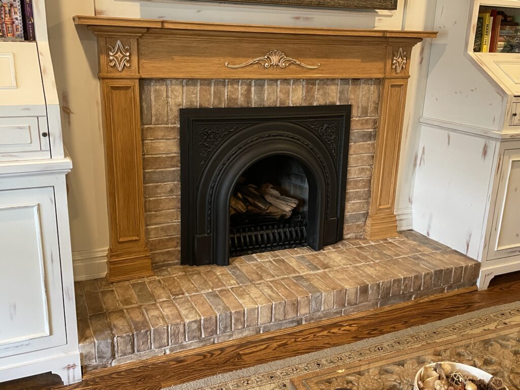 Originally all-white fireplace painted with mortar and multicolor bricks, 2 step color wash for ageing. Surround painted with honey and brown colored paint and glazes.